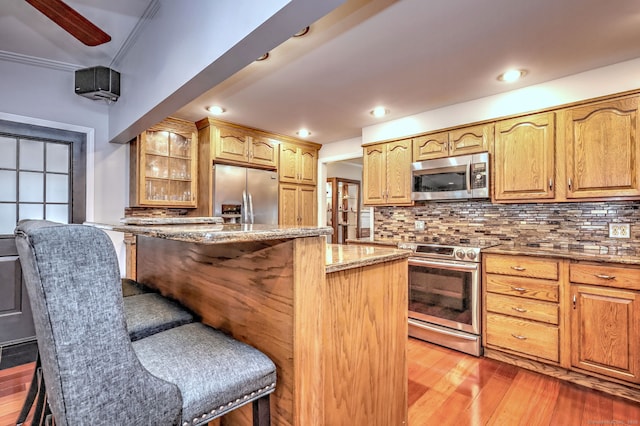 kitchen with decorative backsplash, appliances with stainless steel finishes, light stone countertops, a center island, and a breakfast bar area