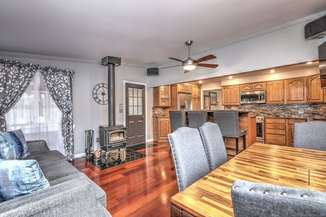 dining room featuring dark hardwood / wood-style flooring, a wood stove, ceiling fan, and ornamental molding