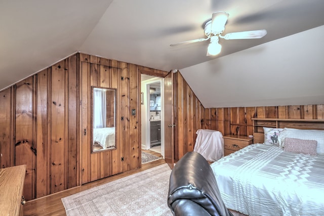 bedroom with ceiling fan, wooden walls, lofted ceiling, and light wood-type flooring