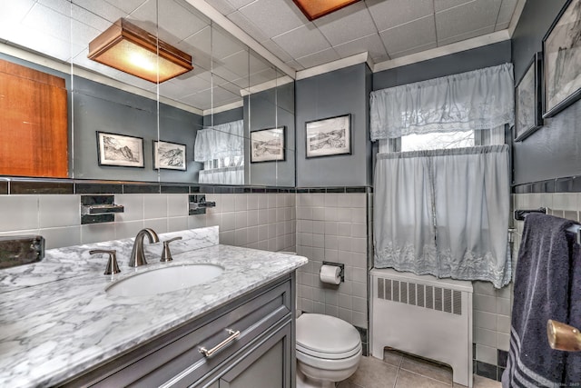 bathroom featuring vanity, tile walls, tile patterned flooring, radiator heating unit, and toilet