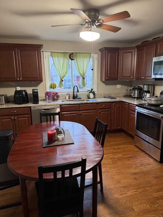 kitchen with appliances with stainless steel finishes, hardwood / wood-style floors, sink, ceiling fan, and light stone countertops