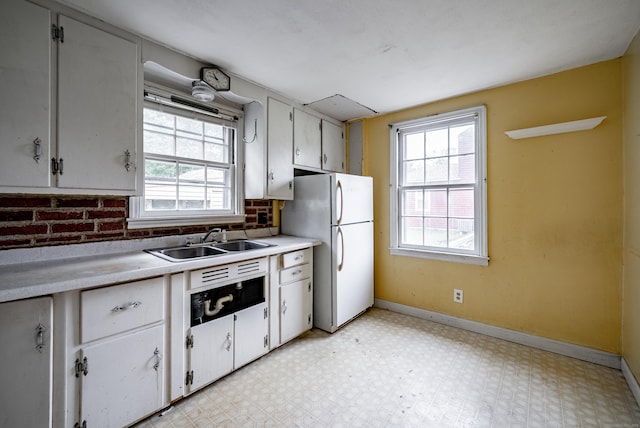 kitchen featuring white cabinets, white fridge, brick wall, and sink