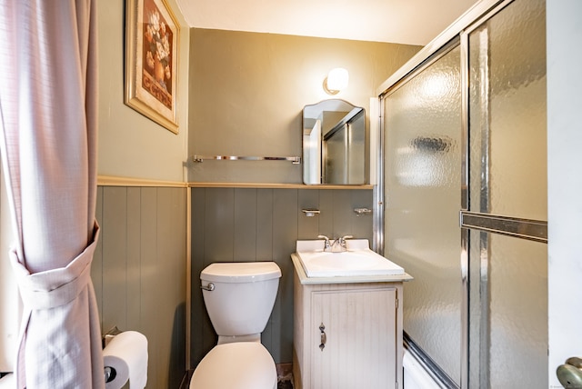 bathroom featuring wooden walls, vanity, an enclosed shower, and toilet