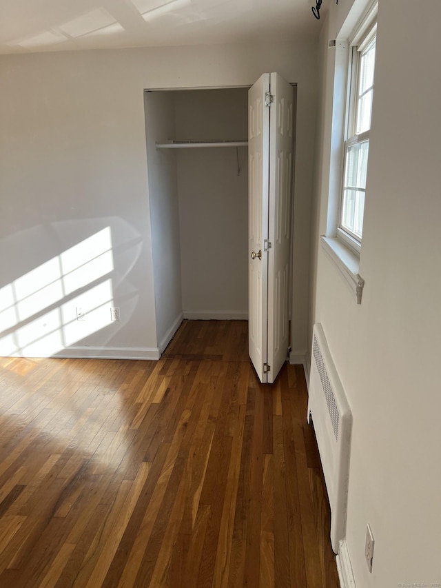 unfurnished bedroom featuring a closet, dark hardwood / wood-style flooring, radiator, and multiple windows