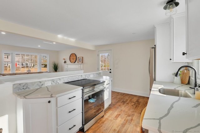 kitchen featuring light stone countertops, a healthy amount of sunlight, sink, white cabinets, and stainless steel range with electric cooktop