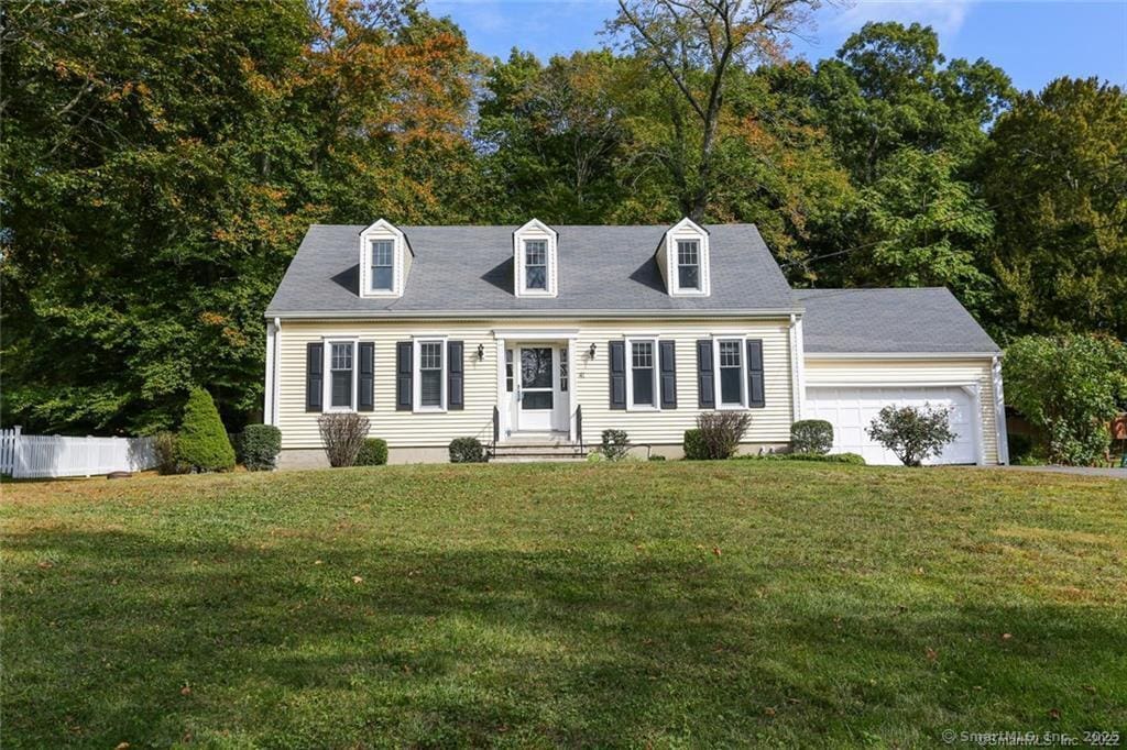 cape cod home featuring a garage and a front lawn