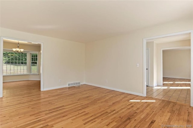 unfurnished room with a notable chandelier and light wood-type flooring