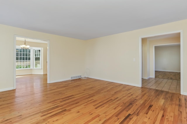 spare room with a notable chandelier and light hardwood / wood-style flooring