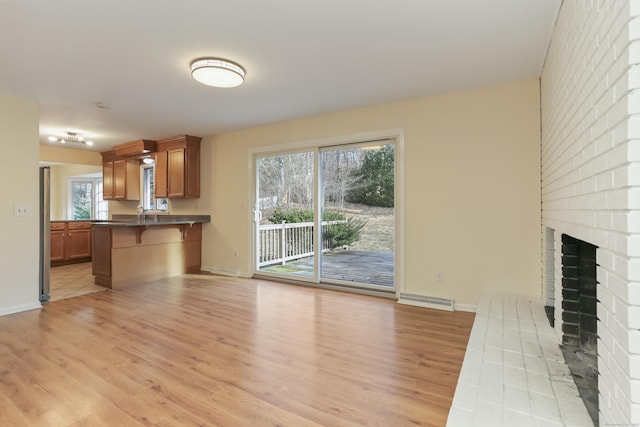 unfurnished living room with light wood-type flooring, a brick fireplace, and a wealth of natural light