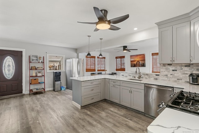 kitchen with appliances with stainless steel finishes, gray cabinetry, kitchen peninsula, pendant lighting, and sink