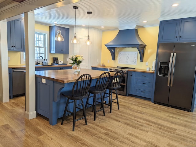 kitchen with blue cabinetry, butcher block countertops, decorative light fixtures, appliances with stainless steel finishes, and light wood-type flooring