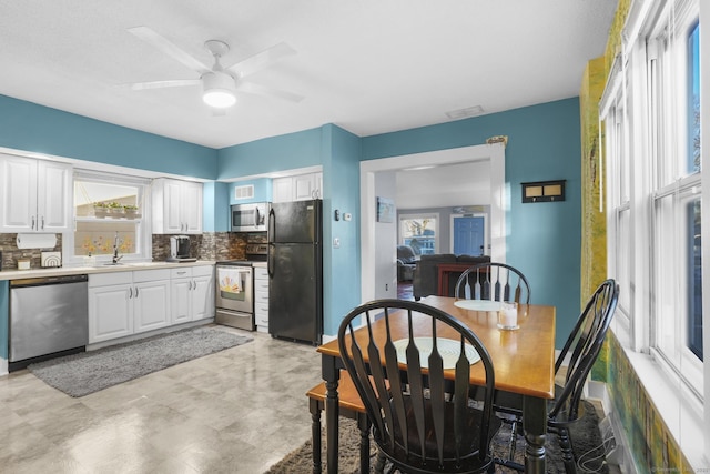 kitchen featuring decorative backsplash, white cabinets, stainless steel appliances, and ceiling fan