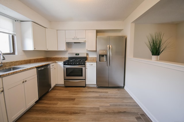 kitchen with stone counters, sink, appliances with stainless steel finishes, light hardwood / wood-style floors, and white cabinetry