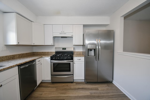 kitchen featuring appliances with stainless steel finishes, a textured ceiling, dark stone countertops, dark hardwood / wood-style floors, and white cabinetry