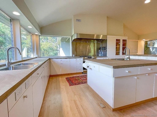 kitchen with sink, white cabinets, vaulted ceiling, and light wood-type flooring