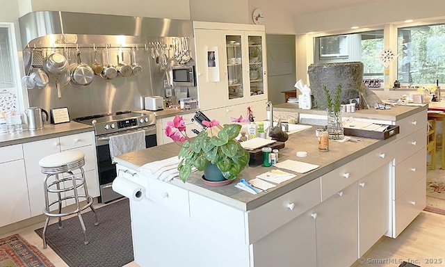 kitchen featuring a kitchen island, white cabinets, wall chimney range hood, and appliances with stainless steel finishes