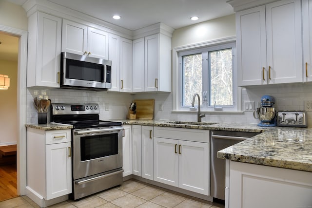 kitchen featuring appliances with stainless steel finishes, white cabinets, a sink, and tasteful backsplash