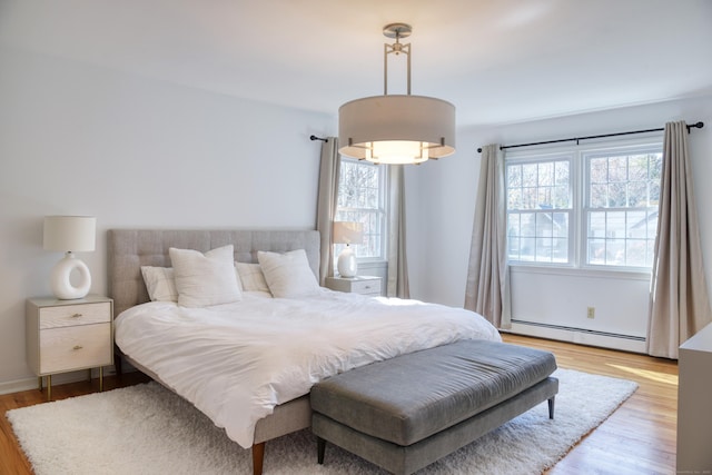 bedroom with a baseboard heating unit and light wood-style flooring