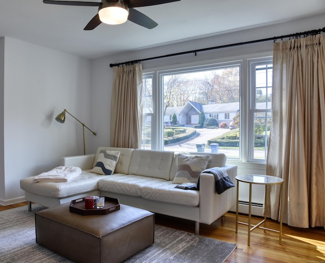 living area featuring a baseboard heating unit, a ceiling fan, and wood finished floors