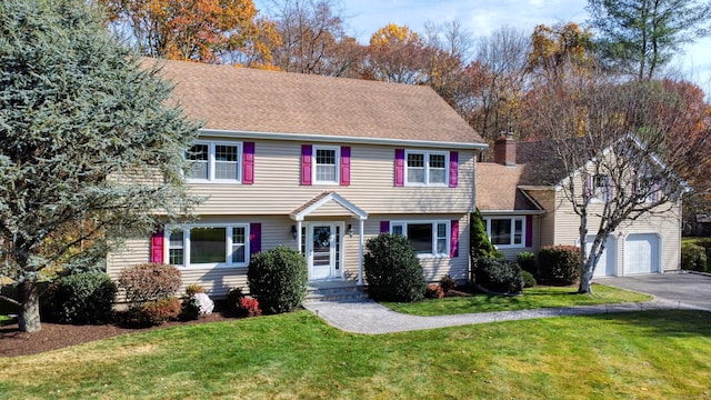 colonial home featuring driveway, roof with shingles, a garage, and a front yard