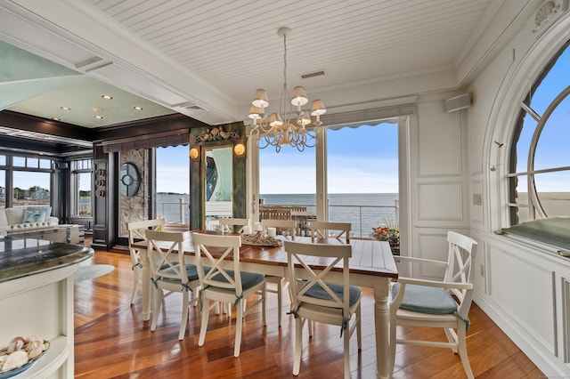 dining area with visible vents, light wood-style flooring, crown molding, a chandelier, and a decorative wall