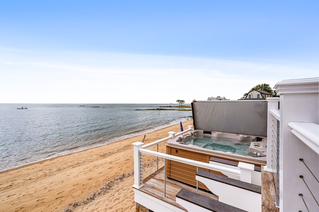 exterior space featuring a water view, a hot tub, and a beach view