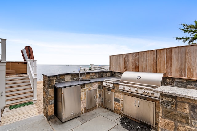 view of patio featuring a water view, an outdoor kitchen, a sink, and area for grilling