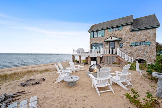 view of patio with an outdoor fire pit, a water view, and a beach view