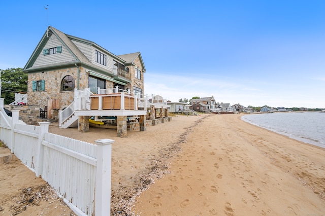 view of front of home featuring a beach view, a water view, fence, stairs, and stone siding