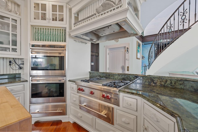 kitchen featuring glass insert cabinets, wood finished floors, custom exhaust hood, stainless steel appliances, and a warming drawer