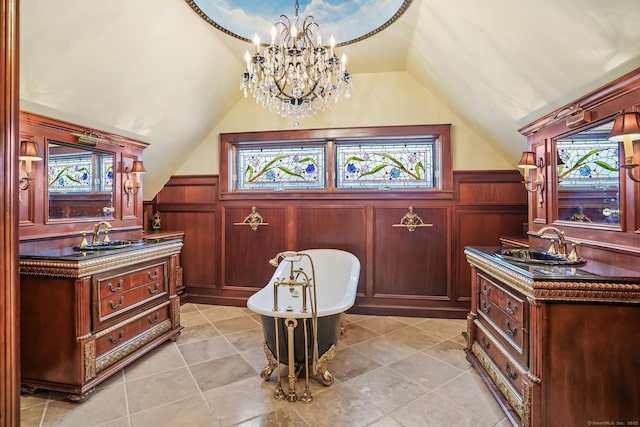 interior space with a wainscoted wall, a freestanding bath, vaulted ceiling, and two vanities