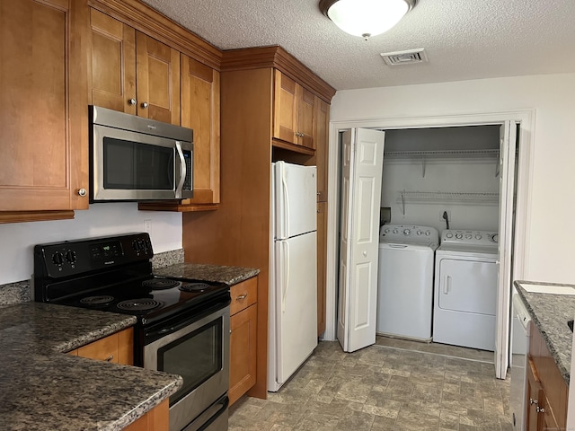 kitchen featuring a textured ceiling, appliances with stainless steel finishes, dark stone countertops, and washer and dryer