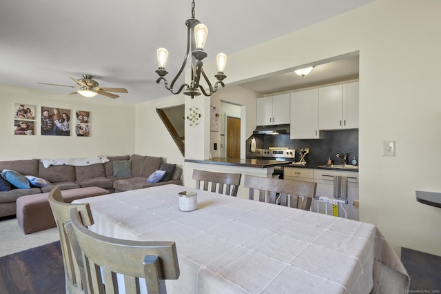 dining space featuring ceiling fan with notable chandelier, sink, and dark wood-type flooring