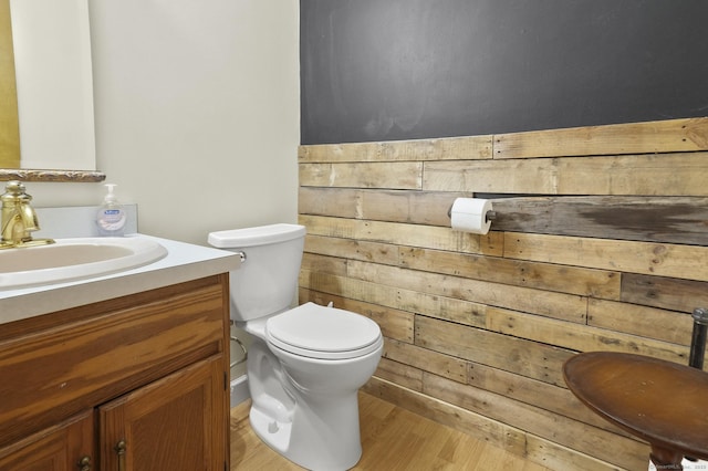 bathroom featuring toilet, wood-type flooring, wooden walls, and vanity