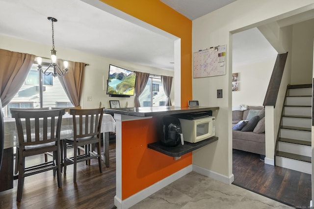 interior space with decorative light fixtures, kitchen peninsula, a notable chandelier, and dark hardwood / wood-style flooring