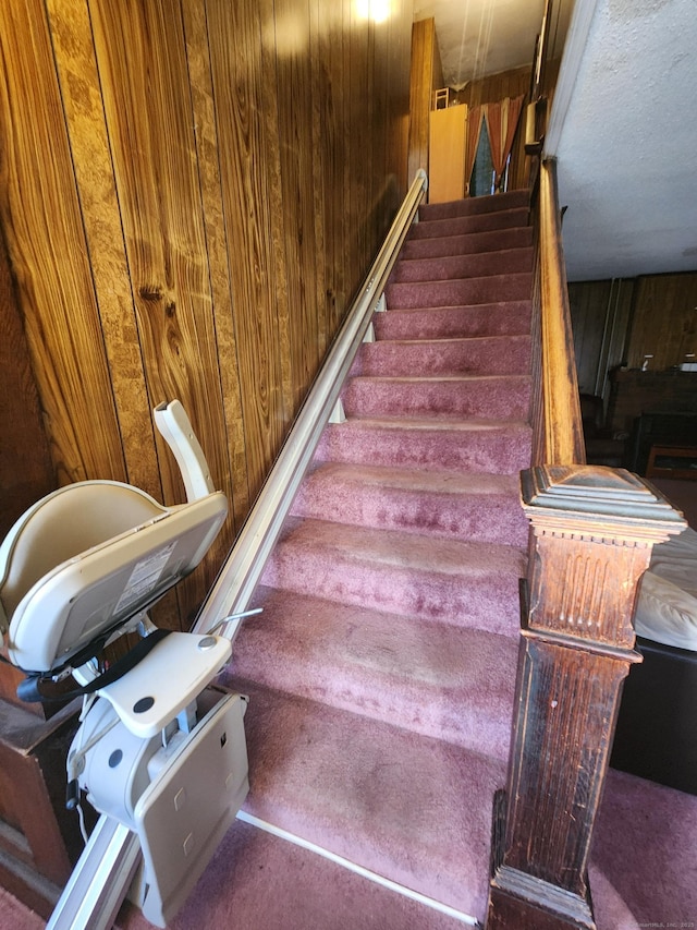 stairway featuring carpet flooring, a textured ceiling, and wooden walls