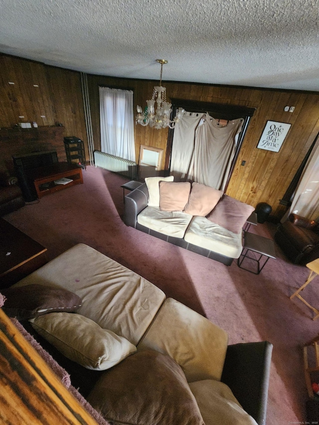 living room featuring carpet flooring, a textured ceiling, an inviting chandelier, and wood walls