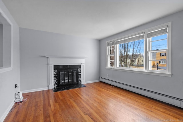 unfurnished living room featuring hardwood / wood-style flooring, baseboard heating, and a tiled fireplace