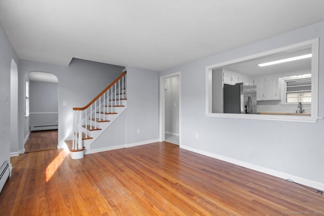 unfurnished living room featuring hardwood / wood-style floors, a baseboard radiator, and sink