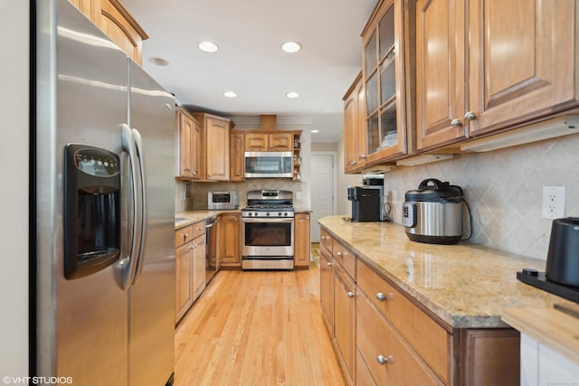 kitchen with light stone counters, backsplash, light wood-type flooring, and appliances with stainless steel finishes