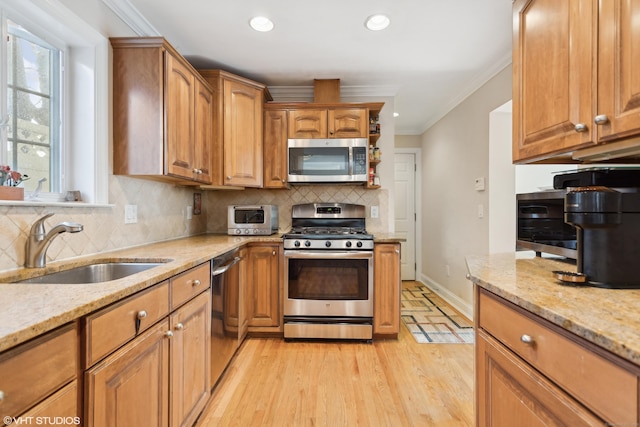 kitchen with ornamental molding, appliances with stainless steel finishes, light stone countertops, and sink