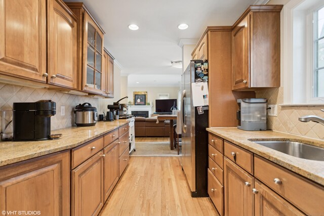 kitchen featuring sink, stainless steel fridge, light stone counters, tasteful backsplash, and light hardwood / wood-style floors