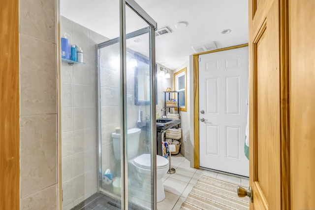 bathroom featuring tile patterned flooring, toilet, a shower with door, and tile walls