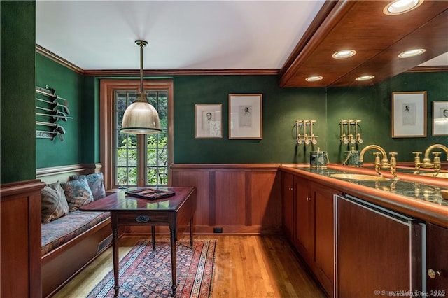 bar with crown molding, sink, light hardwood / wood-style floors, and decorative light fixtures