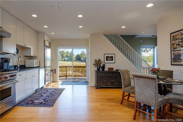 kitchen with white cabinets, sink, light wood-type flooring, premium appliances, and a healthy amount of sunlight