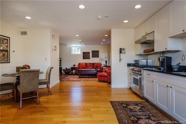 kitchen with high end stove, sink, light hardwood / wood-style flooring, dark stone countertops, and white cabinetry