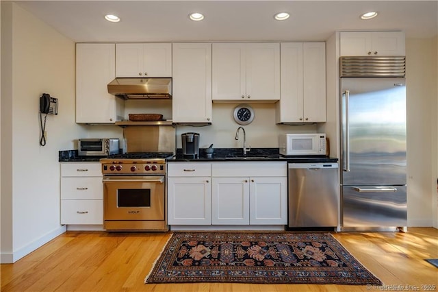 kitchen featuring white cabinetry, sink, premium appliances, dark stone counters, and light wood-type flooring