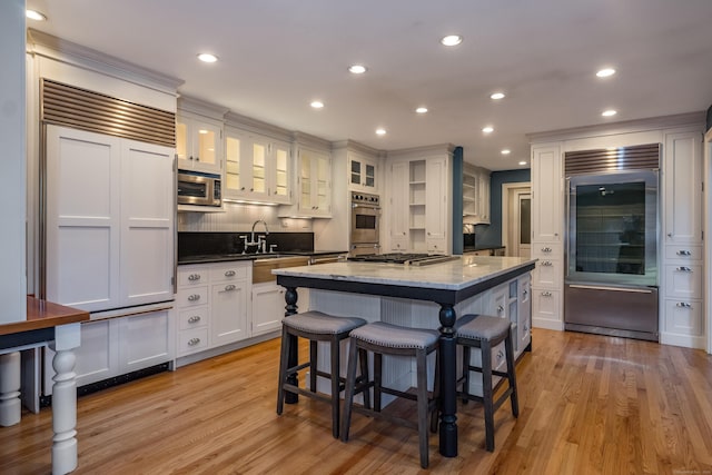 kitchen with built in appliances, white cabinetry, light hardwood / wood-style flooring, dark stone counters, and a kitchen island