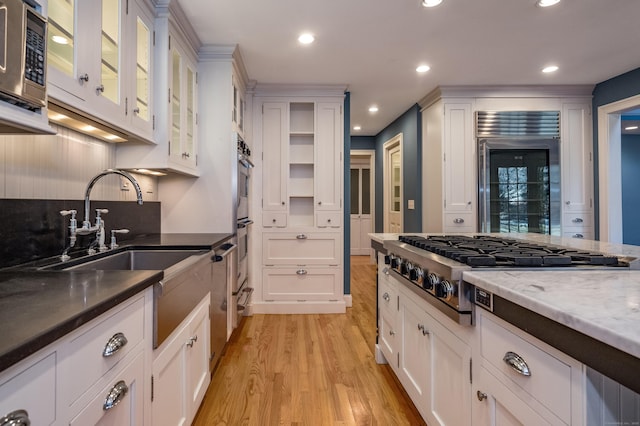 kitchen featuring appliances with stainless steel finishes, dark stone counters, white cabinets, light hardwood / wood-style flooring, and sink