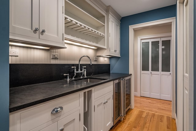 kitchen with wine cooler, dark stone counters, white cabinets, light hardwood / wood-style flooring, and sink